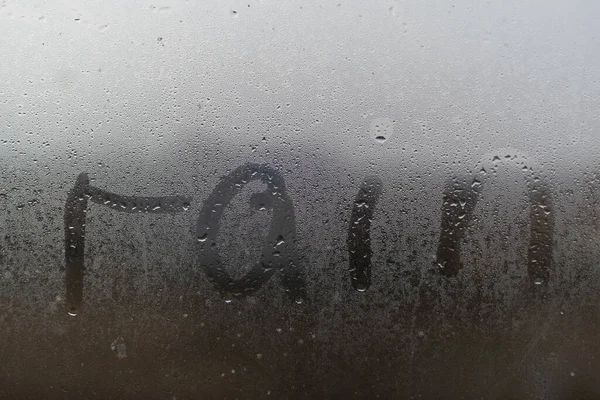 Er staat een woord Regen op het bezwete mistige raam. Waterdruppels condensatie achtergrond van dauw op glas. Wees gelukkig, zelfs bij slecht regenweer buiten het concept. — Stockfoto