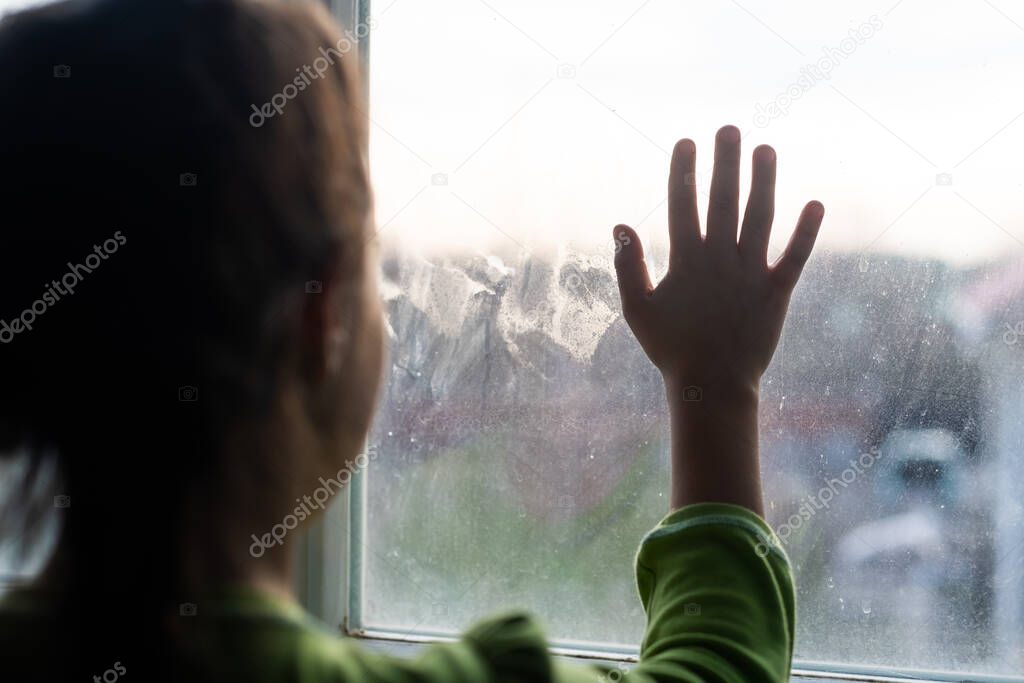 Young girl at window hands pressed against window, pensive or wanting out