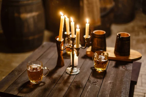 A glass of beer next to a candle on a table — Stock Photo, Image