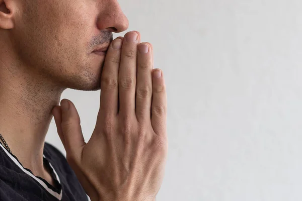 Man bidden. geconcentreerde jonge man in wit overhemd houden handen geklemd in de buurt van gezicht terwijl staande tegen de grijze achtergrond — Stockfoto