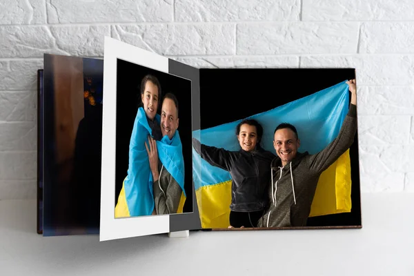 Na mesa branca fotolivro aberto da sessão de fotos da família com bandeira ucraniana — Fotografia de Stock