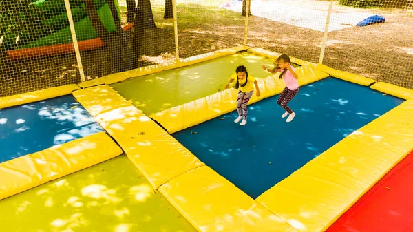 Lilla vackra flickor ha kul utomhus. Hoppa på studsmattan i barn zon. Nöjespark — Stockfoto