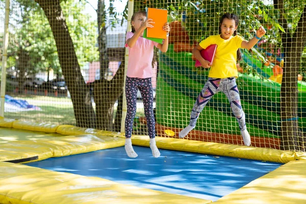 Duas meninas com livros saltar em um trampolim. — Fotografia de Stock