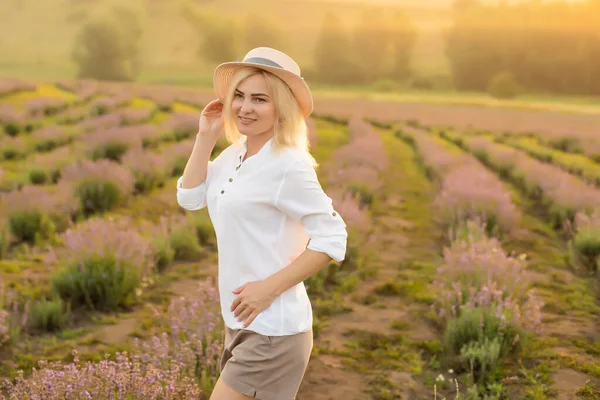 美しい若い健康な女性白いドレスは、夕日の光の下でわら帽子を保持ラベンダー畑を楽しく実行しています — ストック写真