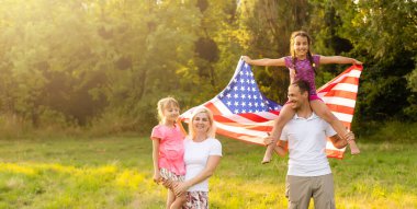 Vatansever bayram. Mutlu aile, gün batımında Amerikan bayrağı taşıyan anne ve kızları. ABD 4 Temmuz 'da bağımsızlığını kutladı.