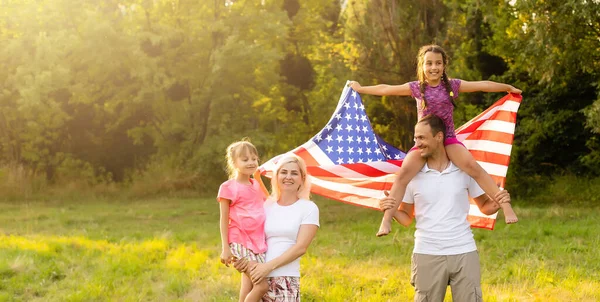 Vacaciones patrióticas. Familia feliz, madre e hijas con bandera americana al aire libre al atardecer. EE.UU. celebra el día de la independencia 4 de julio. — Foto de Stock