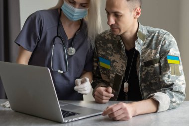 Steteskoplu bir askeri doktor askeri kamuflajlı bir Ukraynalı askeri inceliyor.