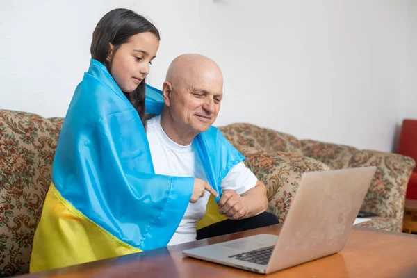 Дідусь і онучка з ноутбуком і прапором України. — стокове фото