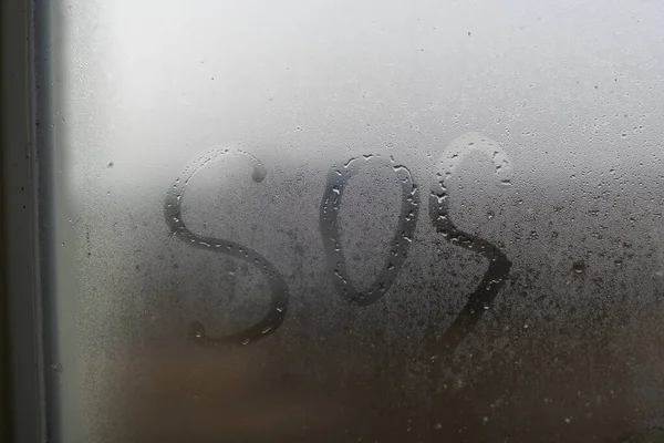 Close-up palavra inscrição SOS em uma janela nebulosa — Fotografia de Stock