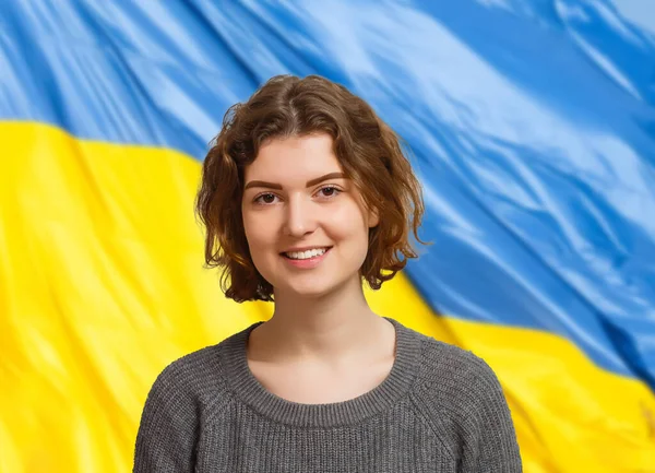 Frau mit Ukraine-Fahne im Hintergrund, die in die Kamera blickt. Konzept, mit der ukrainischen Nation im Krieg gegen Russland zu stehen. — Stockfoto