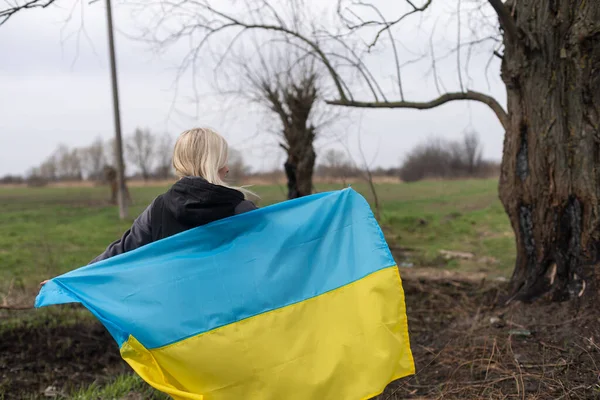 Жінка тримає жовтий і синій прапор України на тлі обгорілого дерева. — стокове фото