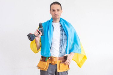 Elinde bir matkapla Ukrayna bayrağıyla duran bir tamirci.