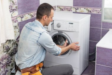 Çalışan tesisatçı çamaşırhanedeki çamaşır makinesini tamir ediyor.
