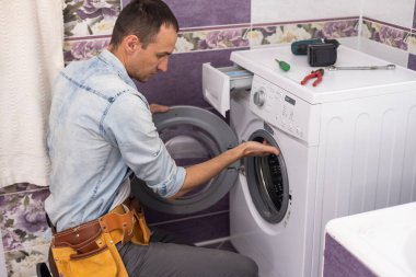 Adam çamaşır makinesini tamir ediyor.