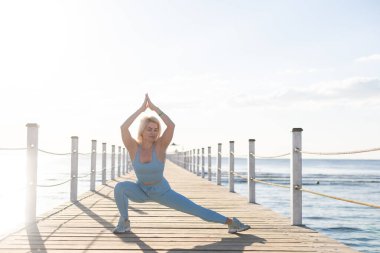 Deniz kenarında duba üzerinde egzersiz yapan bir kadın.