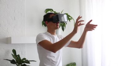 Oturma odasında VR kulaklık takan adam. Ellerinle jestler yapıyorsun. Dinlenme odasında yakışıklı bir adam. Sanal gerçeklik gözlüğü kullan. Yeni teknolojiler. Modern sanal gerçeklik gözlüğü kullanarak bir şeye dokun..