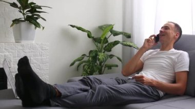 Kanepede oturmuş akıllı telefondan mesaj okuyan olgun bir adam.