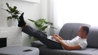 Evdeki kanepede otururken bilgisayarını kullanan adamın portresi.