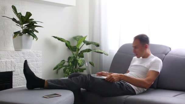 Porträt eines Mannes, der zu Hause auf einer Couch sitzt und Laptop benutzt — Stockvideo