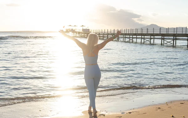 Vista laterale di donna magra in abiti sportivi camminare vicino alle onde calme del mare trascorrere il fine settimana mattina per l'allenamento nella natura, bella femmina in tuta da ginnastica che sceglie il luogo per lo stretching — Foto Stock