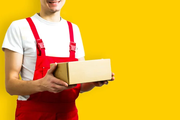 Mag szczęśliwy młody dostawca człowiek w czerwonej czapce stojący z paczki skrzynki pocztowej izolowane na żółtym tle — Zdjęcie stockowe