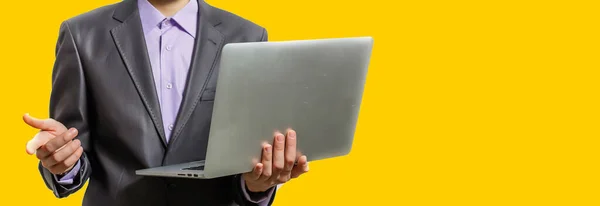 Работать с радостью. Красивый молодой человек, использующий ноутбук и смотрящий в камеру с улыбкой, стоя на жёлтом фоне — стоковое фото