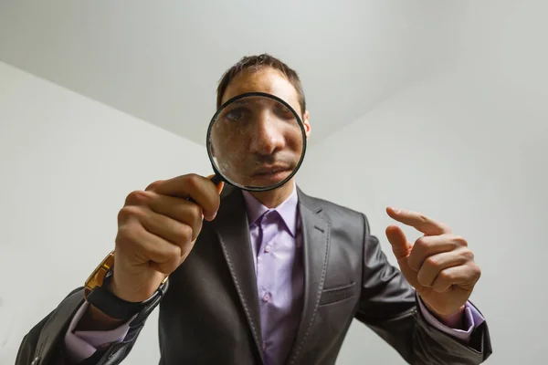 Young male detective holding magnifying glass by right eye while standing in front of camera in isolation — Stock Photo, Image