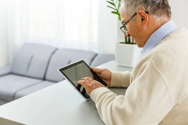 Oturma odasındaki masada dijital tablet kullanan yakışıklı, neşeli, son sınıf öğrencisi. Boş zaman aktiviteleri, zaman geçirme, mutlu emeklilik ve yaşlılar yaşam tarzı konsepti — Stok fotoğraf