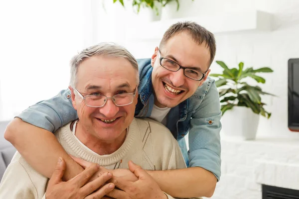 Staruszek na wózku i jego syn. Mężczyzna przytula starszego ojca. Są szczęśliwi i uśmiechnięci. — Zdjęcie stockowe