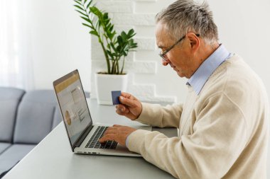 Bilgisayardaki kıdemli adam online alışveriş için kredi kartıyla ödeme yapıyor.
