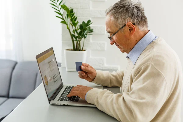 Uomo anziano al computer portatile che paga con carta di credito per lo shopping online — Foto Stock