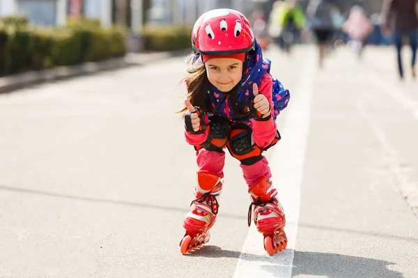 Engraçado menina bonita em patins em capacete montando em um parque. Conceito de estilo de vida saudável — Fotografia de Stock
