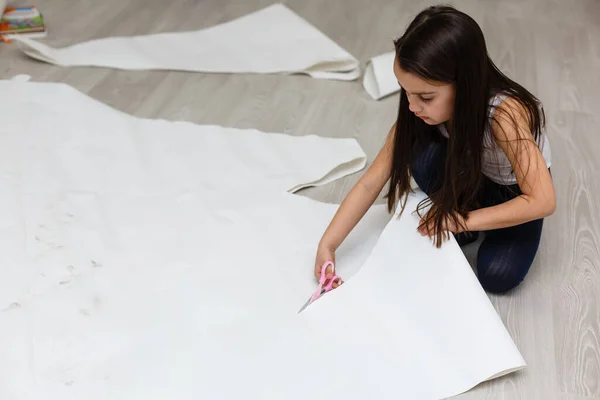 Küçük kız otururken makas kullanarak kağıt kesiyor. — Stok fotoğraf