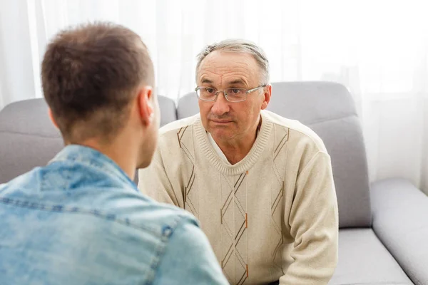 Young man sitting on a sofa smiling and talking with his grandfather — Stock Photo, Image