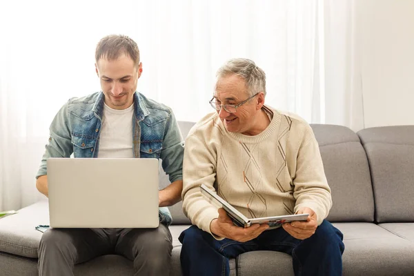 Yaşlı baba albüm okuyor ve oğlu tablet kullanıyor. — Stok fotoğraf