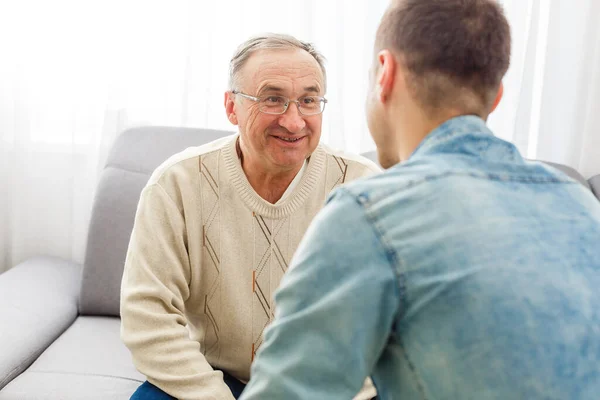 Glad pensionerad man och vuxen son pratar hemma — Stockfoto