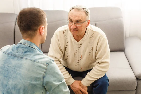 Ung man sitter på en soffa ler och pratar med sin farfar — Stockfoto