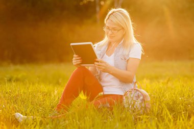 Parkta oturup kitap okuyan memnun bir kadın.