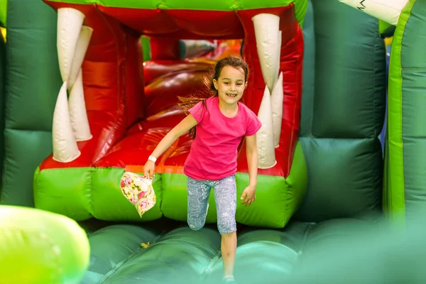 Linda niña preescolar divertida en un colorido, saltando y rebotando en un castillo inflable divirtiéndose en una fiesta de cumpleaños de niños en un parque infantil en verano —  Fotos de Stock