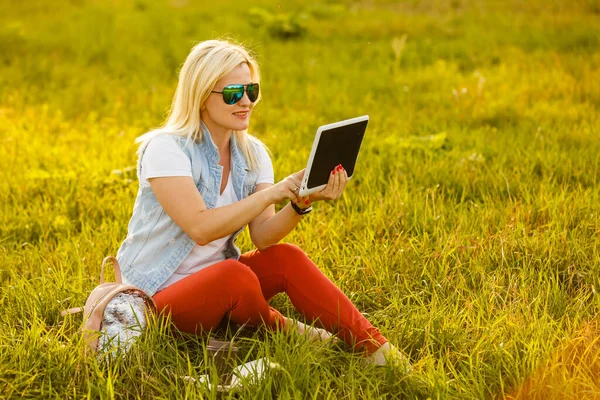 Kobieta na zielonej trawie z tabletką podczas pikniku w parku — Zdjęcie stockowe