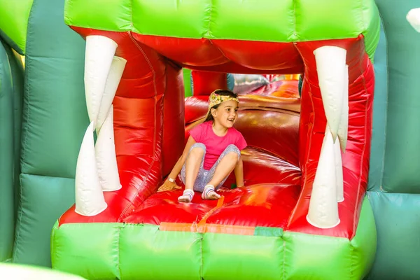 Menina pré-escolar engraçada bonito em um colorido, pulando e saltando em um castelo inflável se divertindo em uma festa de aniversário de crianças em um parque infantil no verão — Fotografia de Stock
