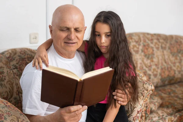 Feliz abuelo y nieta leyendo el libro juntos en casa. De cerca.. —  Fotos de Stock