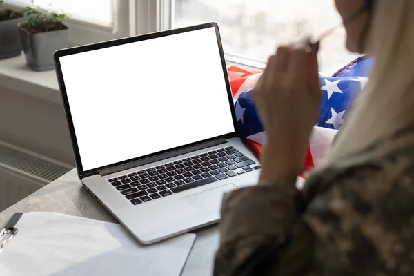 Militar gesto en la oficina cerca de la computadora portátil con pantalla en blanco, bandera de EE.UU.. — Foto de Stock
