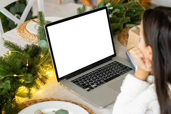 Маленька дівчинка за допомогою ноутбука з чистим білим екраном копіювального простору телефонує Санта Клаусу або родичам або навчається в Інтернеті сидячи за столом на Різдвяних святах вдома. — стокове фото