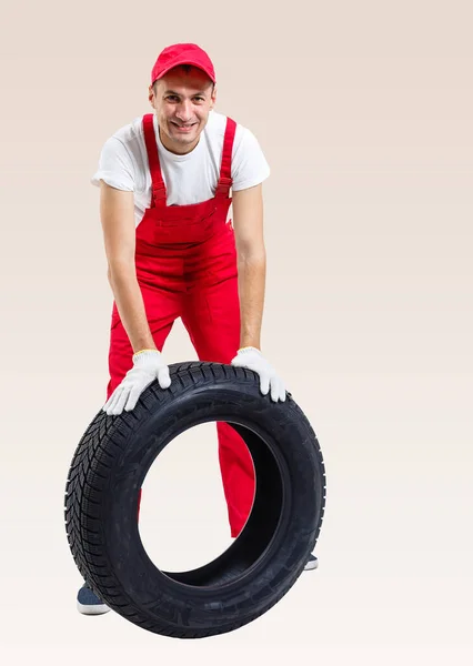 Mecânico segurando um pneu na garagem de reparo. substituição de pneus de inverno e verão. — Fotografia de Stock