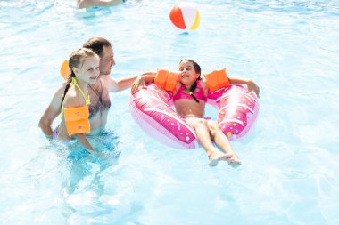 Aktif bir baba çocuklarına tropik tatil köyünde havuzda yüzmeyi öğretiyor. Yaz tatilleri ve spor konsepti