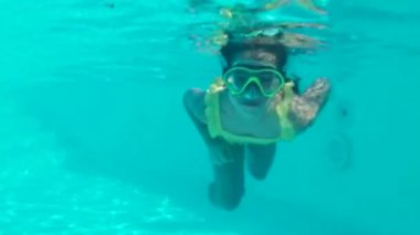 Küçük kız su altında panoramik bir maskeyle yüzüyor. Bir çocuk şnorkelle yüzüyor. Köpükler bebeğin etrafını sardı..