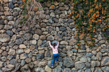 Genç bir kız bir tepenin tepesindeki kayaların üzerinden tırmanıyor.