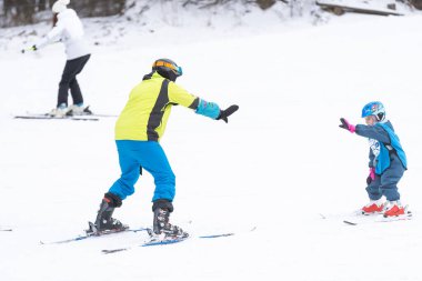 Eğitmen ve küçük çocuk kayak yapıyor. Kasklı, yeni yürümeye başlayan bir çocuk. Küçük çocuklar için kayak dersi. Kış sporu. Küçük kayakçı.