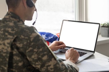 Ordu mensubu laptopun yanında boş ekran ABD bayrağıyla el kol hareketi yapıyor..